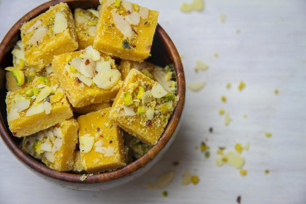 pexels photo 7182054 7182054 Top view of delicious Indian besan barfi garnished with almonds and pistachios, served in a wooden bowl.